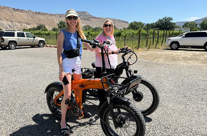 Two friends with orange and black eTrikes at a Palisade vineyard